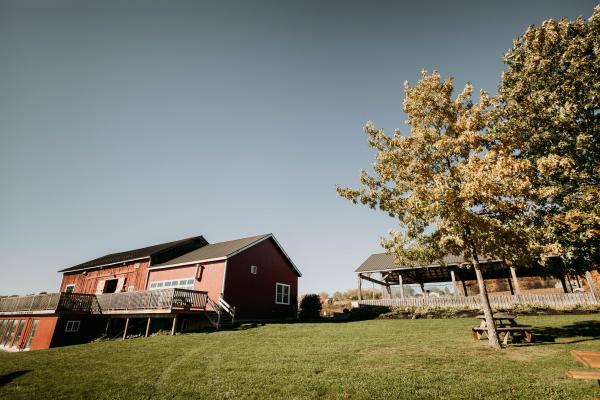 Photo of a red barn like building to the left and a tree to the right with another building in the background
