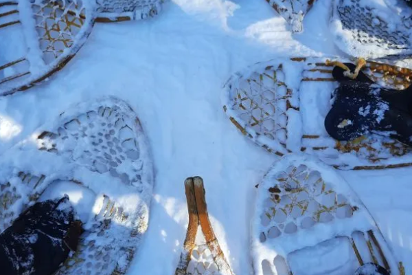 People wearing snow shoes putting their feet in a circle, on top of snow.