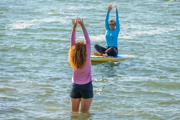 Woman practicing yoga on a paddleboard while instructor stands in the water teaching.
