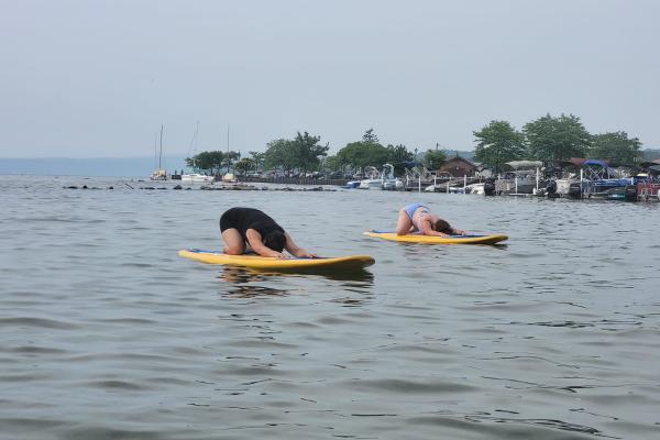 SUP Yoga Class on Sodus Bay. Two people do child's pose on paddleboards.