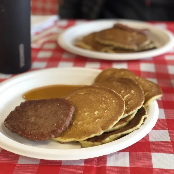 A two plates of fresh pancakes and a sausage pattie. 