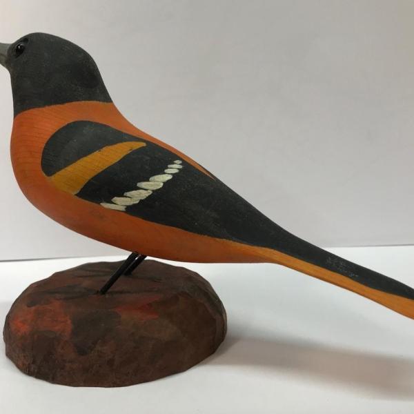Wood carving of a Baltimore Oriole perched on a wood rock.